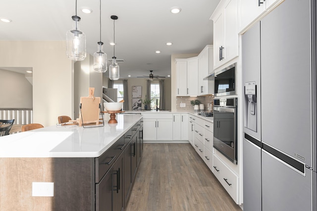 kitchen featuring dark wood-type flooring, hanging light fixtures, an island with sink, appliances with stainless steel finishes, and white cabinetry