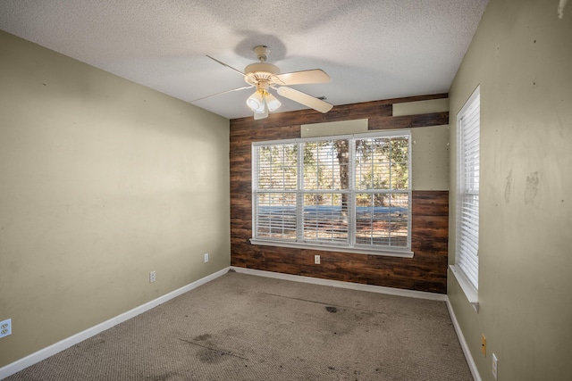 carpeted empty room featuring ceiling fan, wood walls, and a textured ceiling