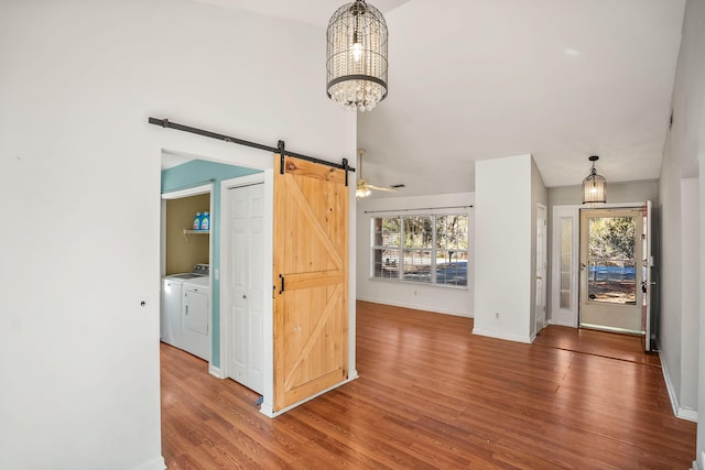 interior space with hardwood / wood-style floors, an inviting chandelier, a barn door, and washing machine and clothes dryer