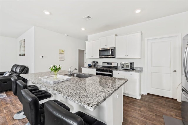 kitchen featuring light stone counters, an island with sink, white cabinets, and appliances with stainless steel finishes