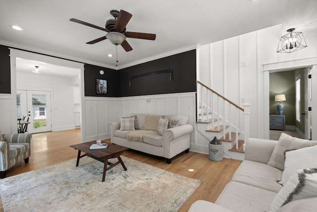 living room with stairs, light wood-style flooring, ceiling fan, crown molding, and a decorative wall