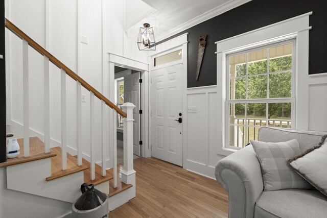 entryway featuring a decorative wall, stairs, a chandelier, light wood-style floors, and ornamental molding