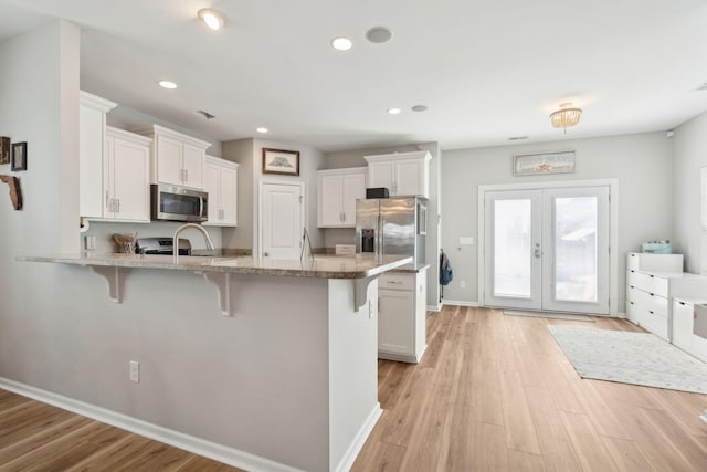 kitchen featuring a breakfast bar, appliances with stainless steel finishes, kitchen peninsula, white cabinets, and french doors