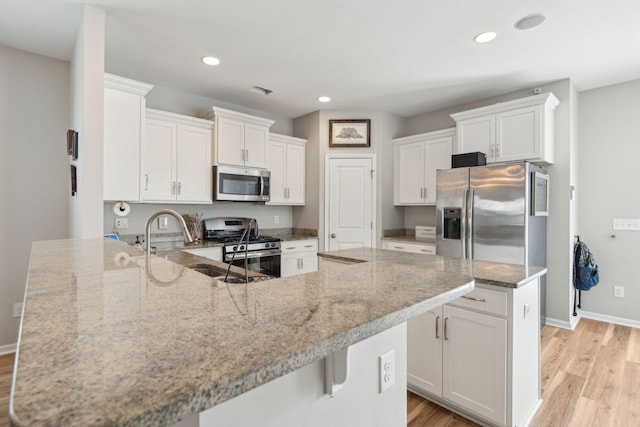 kitchen featuring stainless steel appliances, white cabinetry, light stone counters, and kitchen peninsula