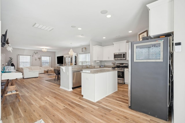 kitchen with appliances with stainless steel finishes, hanging light fixtures, a center island, white cabinets, and kitchen peninsula