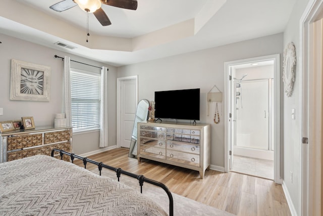 bedroom featuring ceiling fan, a tray ceiling, ensuite bath, and light hardwood / wood-style flooring