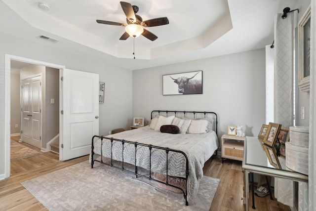 bedroom featuring a raised ceiling, ceiling fan, and light wood-type flooring