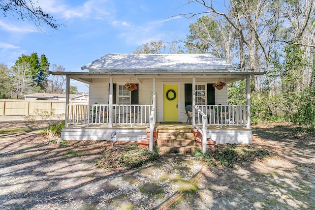 bungalow featuring covered porch, metal roof, and fence