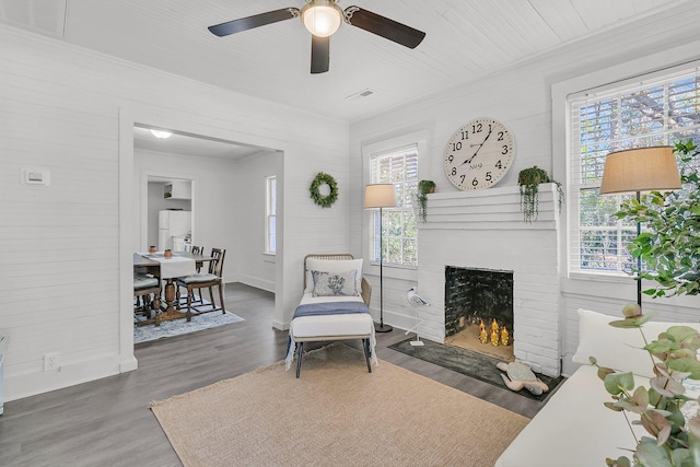 living area featuring visible vents, a brick fireplace, ceiling fan, ornamental molding, and wood finished floors