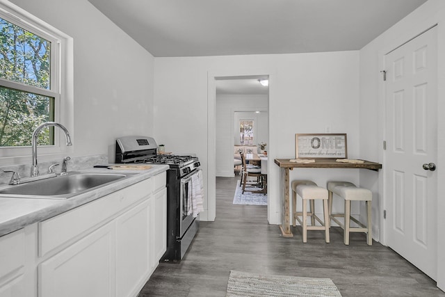 kitchen with a sink, white cabinetry, light countertops, gas range, and dark wood-style flooring