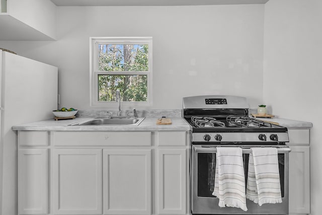 kitchen featuring stainless steel range with gas cooktop, light countertops, freestanding refrigerator, white cabinetry, and a sink