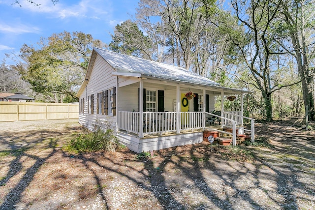 view of front facade featuring fence, covered porch, and metal roof