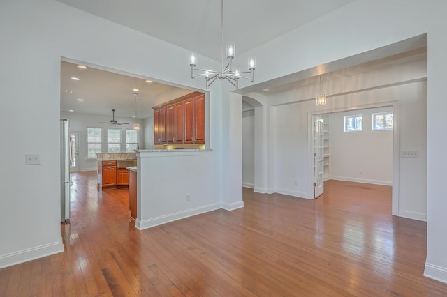 unfurnished living room featuring ceiling fan with notable chandelier and hardwood / wood-style flooring