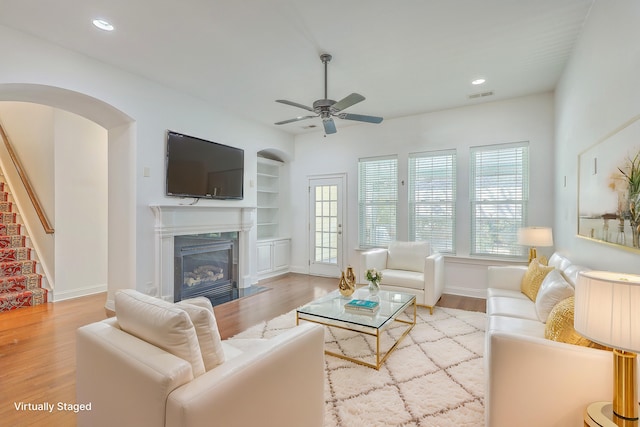 living room featuring ceiling fan, built in shelves, and light wood-type flooring