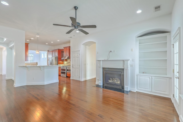 unfurnished living room featuring ceiling fan, built in shelves, and dark wood-type flooring