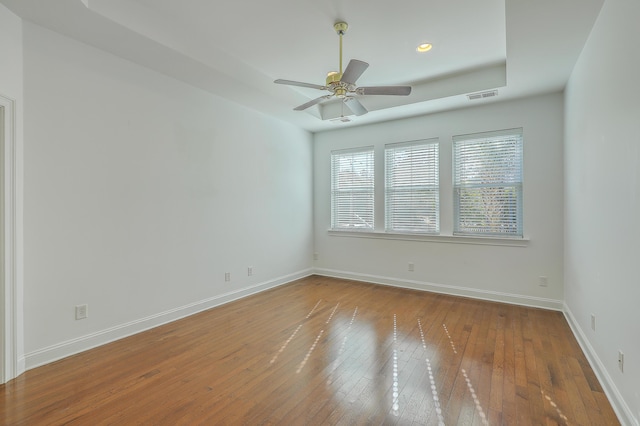 empty room featuring ceiling fan, wood-type flooring, and a raised ceiling