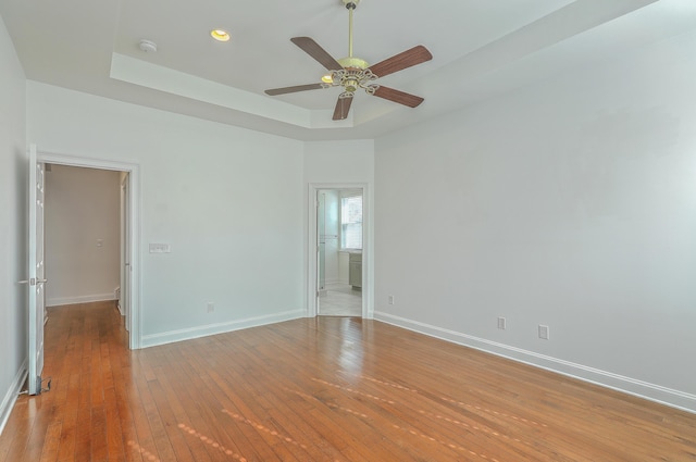 empty room featuring ceiling fan, a tray ceiling, and light wood-type flooring