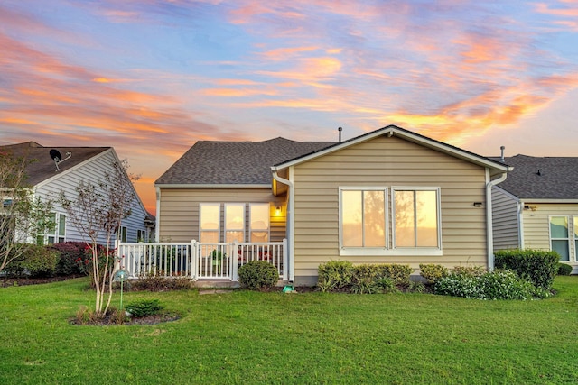 back house at dusk featuring a lawn and a porch