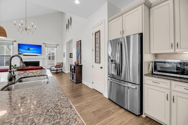 kitchen featuring open floor plan, stainless steel appliances, a sink, light wood-style flooring, and a notable chandelier