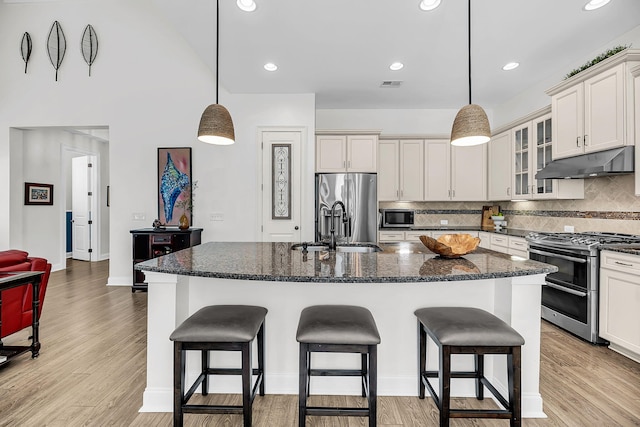 kitchen with visible vents, a kitchen bar, stainless steel appliances, under cabinet range hood, and a sink