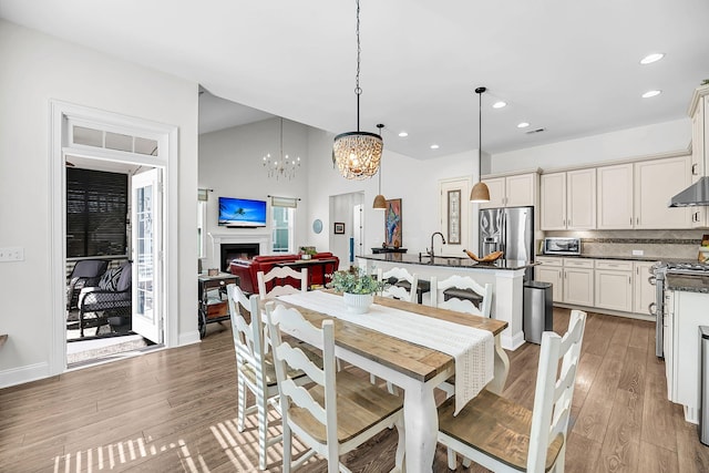 dining room with a fireplace, wood finished floors, recessed lighting, lofted ceiling, and an inviting chandelier