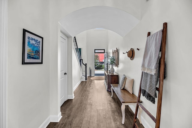 corridor with baseboards, stairway, dark wood-style floors, and arched walkways