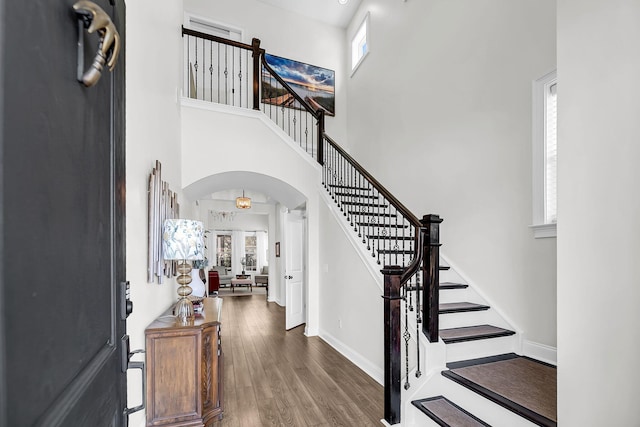 entrance foyer featuring arched walkways, a healthy amount of sunlight, stairs, and wood finished floors