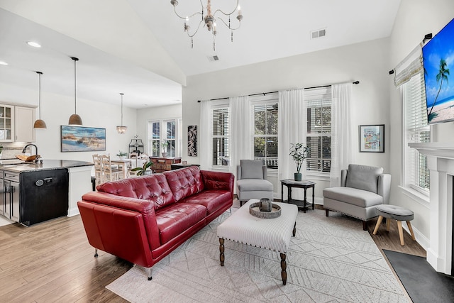 living room with vaulted ceiling, baseboards, light wood finished floors, visible vents, and a notable chandelier