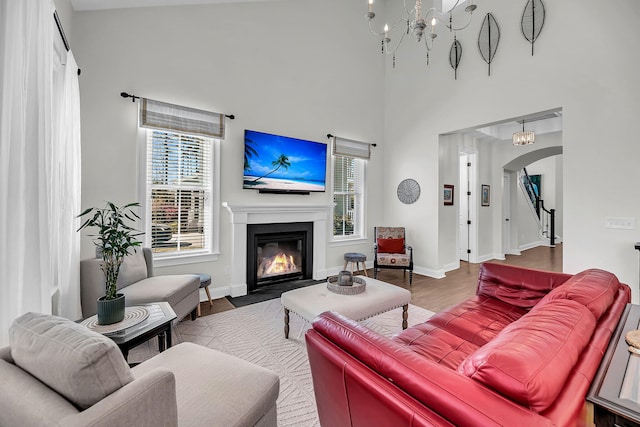 living room featuring a notable chandelier, a fireplace with flush hearth, wood finished floors, baseboards, and arched walkways