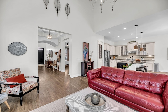 living area featuring dark wood-style floors, baseboards, arched walkways, a towering ceiling, and recessed lighting
