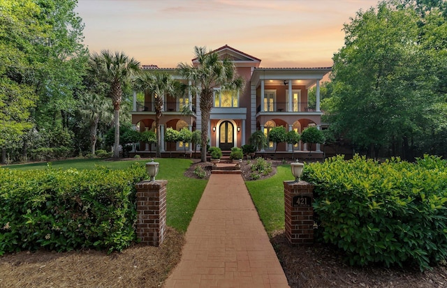 view of front of house with a yard, a balcony, french doors, and stucco siding