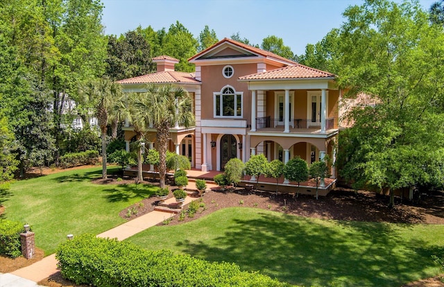 mediterranean / spanish home with a balcony, stucco siding, a front yard, a tile roof, and covered porch