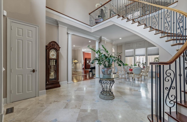 entrance foyer featuring crown molding, decorative columns, stairway, a high ceiling, and baseboards
