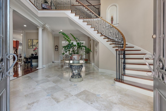foyer entrance with crown molding, a towering ceiling, ornate columns, and stairs