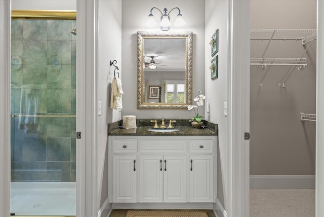 bathroom featuring a walk in closet, baseboards, a shower stall, and vanity