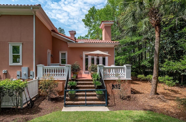rear view of house with a tiled roof, a wooden deck, stucco siding, and a chimney