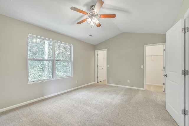 unfurnished bedroom with vaulted ceiling, a spacious closet, a closet, light carpet, and ceiling fan