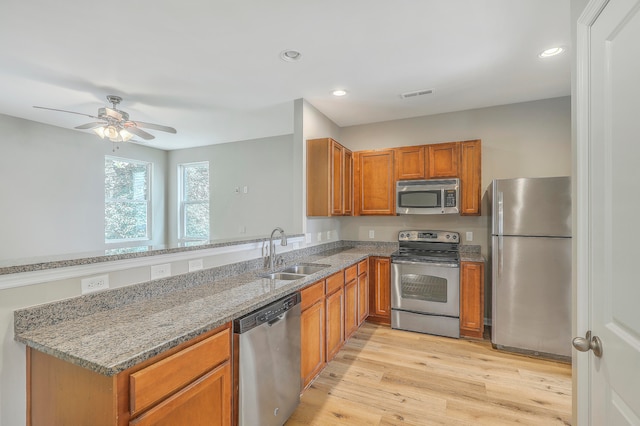 kitchen with dark stone countertops, sink, ceiling fan, appliances with stainless steel finishes, and light hardwood / wood-style floors