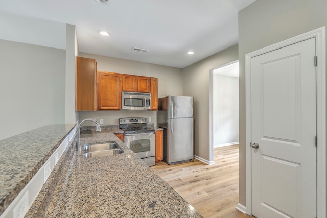 kitchen featuring stainless steel appliances, sink, dark stone countertops, and light hardwood / wood-style floors