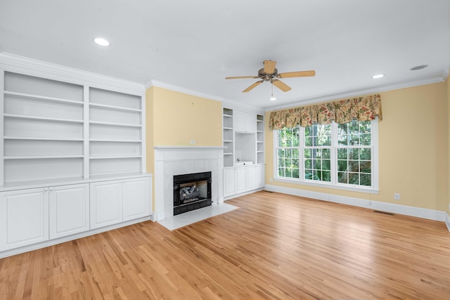 unfurnished living room with light wood-type flooring, ornamental molding, built in features, ceiling fan, and a fireplace