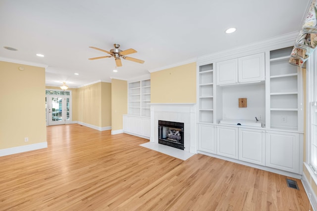 unfurnished living room featuring a tile fireplace, built in features, ornamental molding, ceiling fan, and light wood-type flooring