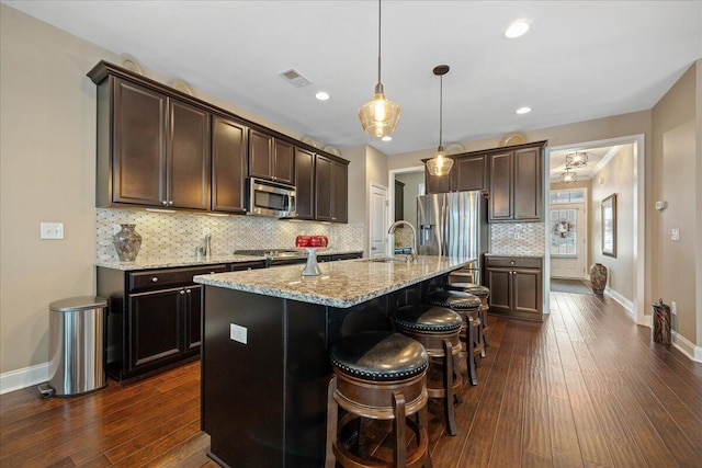 kitchen featuring a breakfast bar, hanging light fixtures, appliances with stainless steel finishes, a kitchen island with sink, and light stone countertops