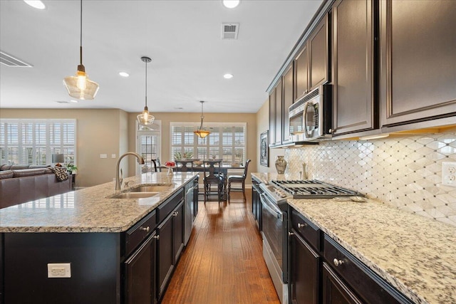 kitchen featuring stainless steel appliances, a sink, a center island with sink, and pendant lighting