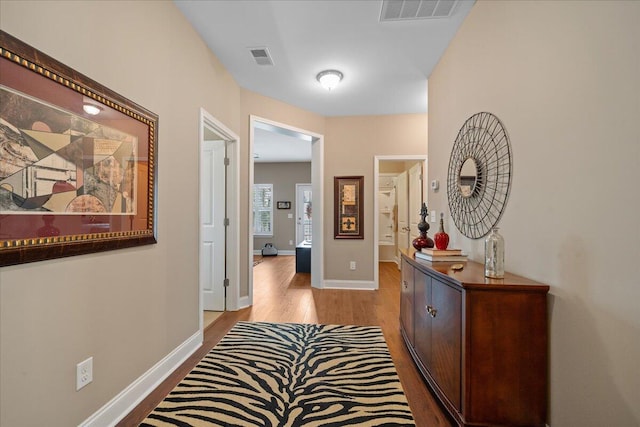 hall featuring baseboards, visible vents, and light wood finished floors