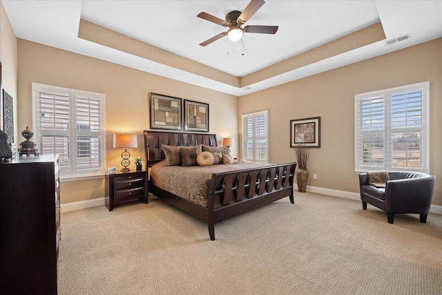 bedroom featuring baseboards, visible vents, a tray ceiling, and multiple windows