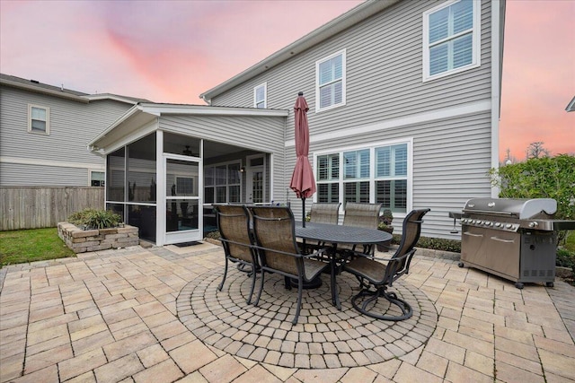 view of patio featuring a sunroom, a grill, fence, and outdoor dining space