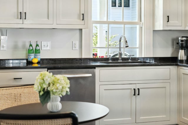 kitchen with stainless steel dishwasher, dark countertops, white cabinets, and a sink