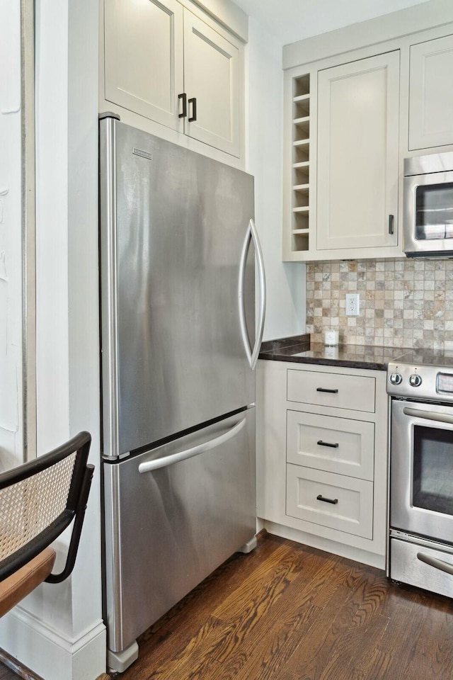 kitchen featuring dark countertops, backsplash, dark wood-type flooring, appliances with stainless steel finishes, and white cabinetry