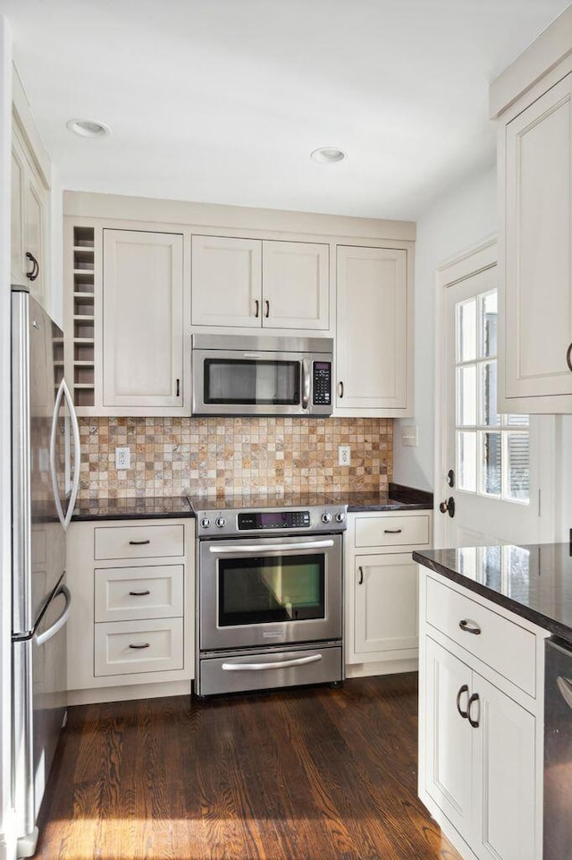 kitchen with backsplash, dark stone counters, stainless steel appliances, dark wood-style floors, and white cabinetry