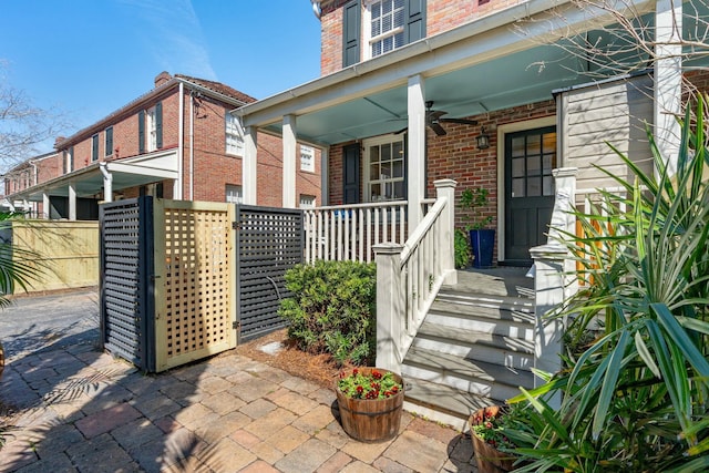 property entrance with brick siding, a porch, and fence